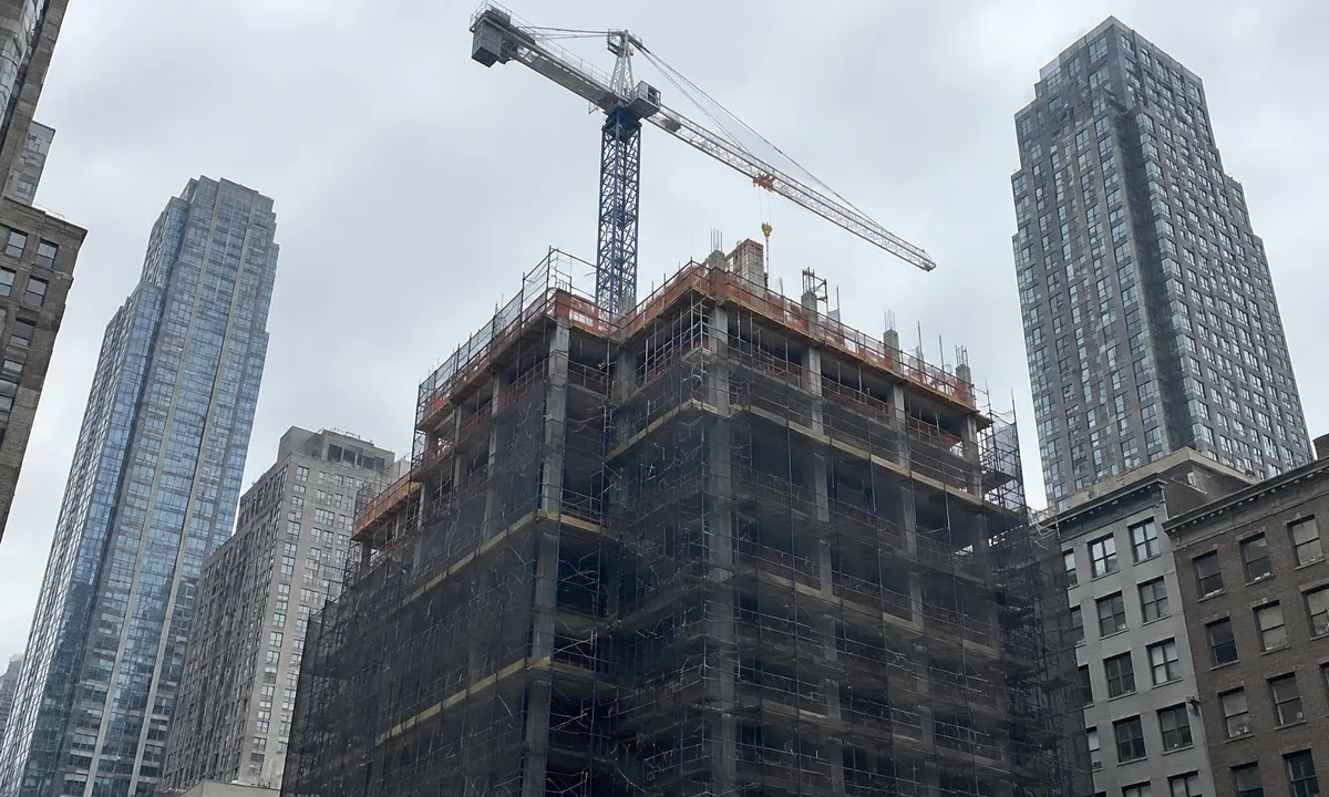 A mid-rise building under construction in New York City, with scaffolding and a tower crane