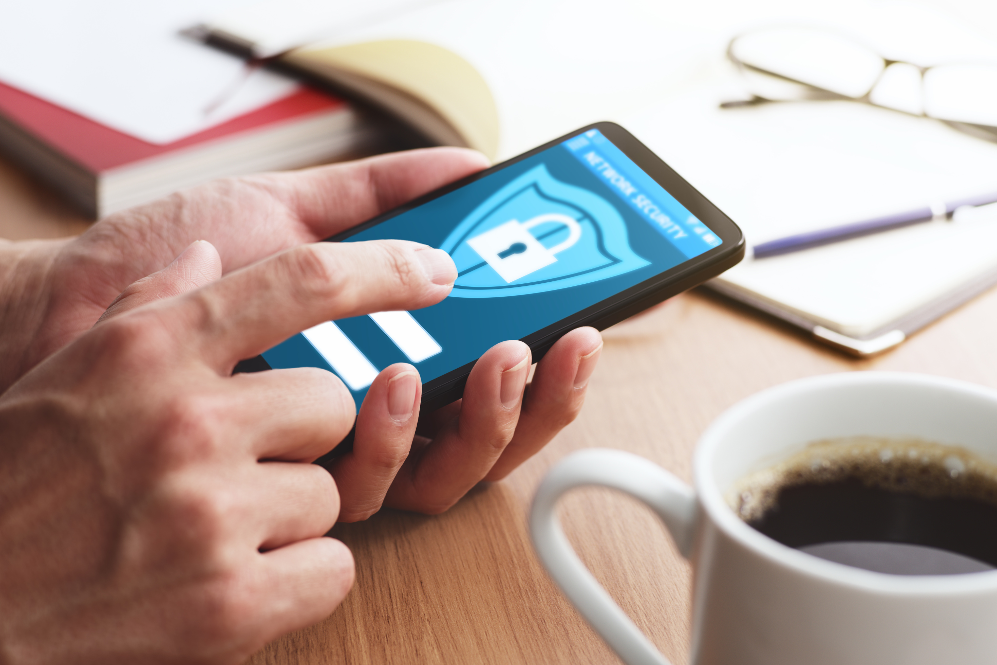 A person holding a smartphone with a security app open, while a fingerprint scanner and a security token are visible nearby